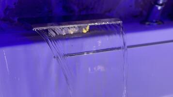 Een helder glas water met een stromende waterstraal, geplaatst op een oppervlak met een blauwe tint.