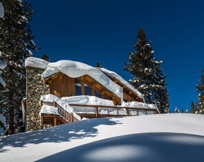 Een besneeuwde lodge met een stenen gevel en houten balken, omringd door sneeuwzware bomen.