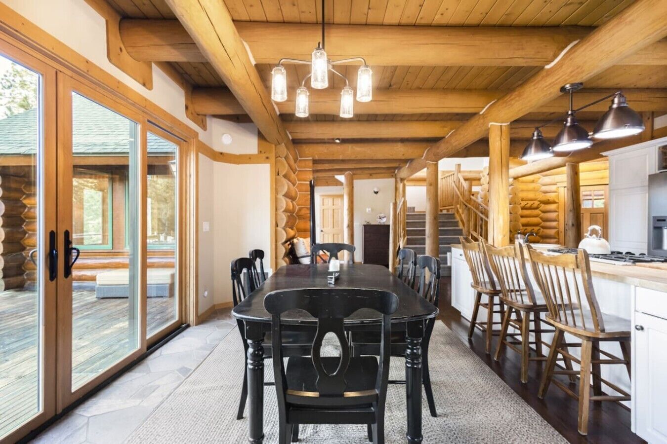 Interior de una cabaña de troncos con comedor, cocina y ventanas amplias.