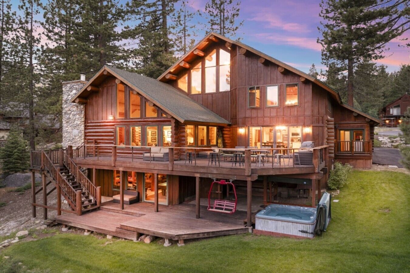 A large log cabin with a deck, outdoor seating, and a hot tub.