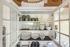 Une cuisine avec des placards ouverts où sont exposés différents plats et ustensiles.