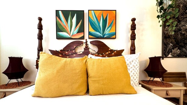 A bed with two yellow pillows, a wooden headboard, and two wall-mounted paintings. - Charming Boho 2 bedroom in Miramar - Back 2B (San Juan)