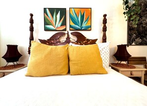 Una cama con dos almohadones amarillos, un cabecero de madera y dos cuadros colgados en la pared.