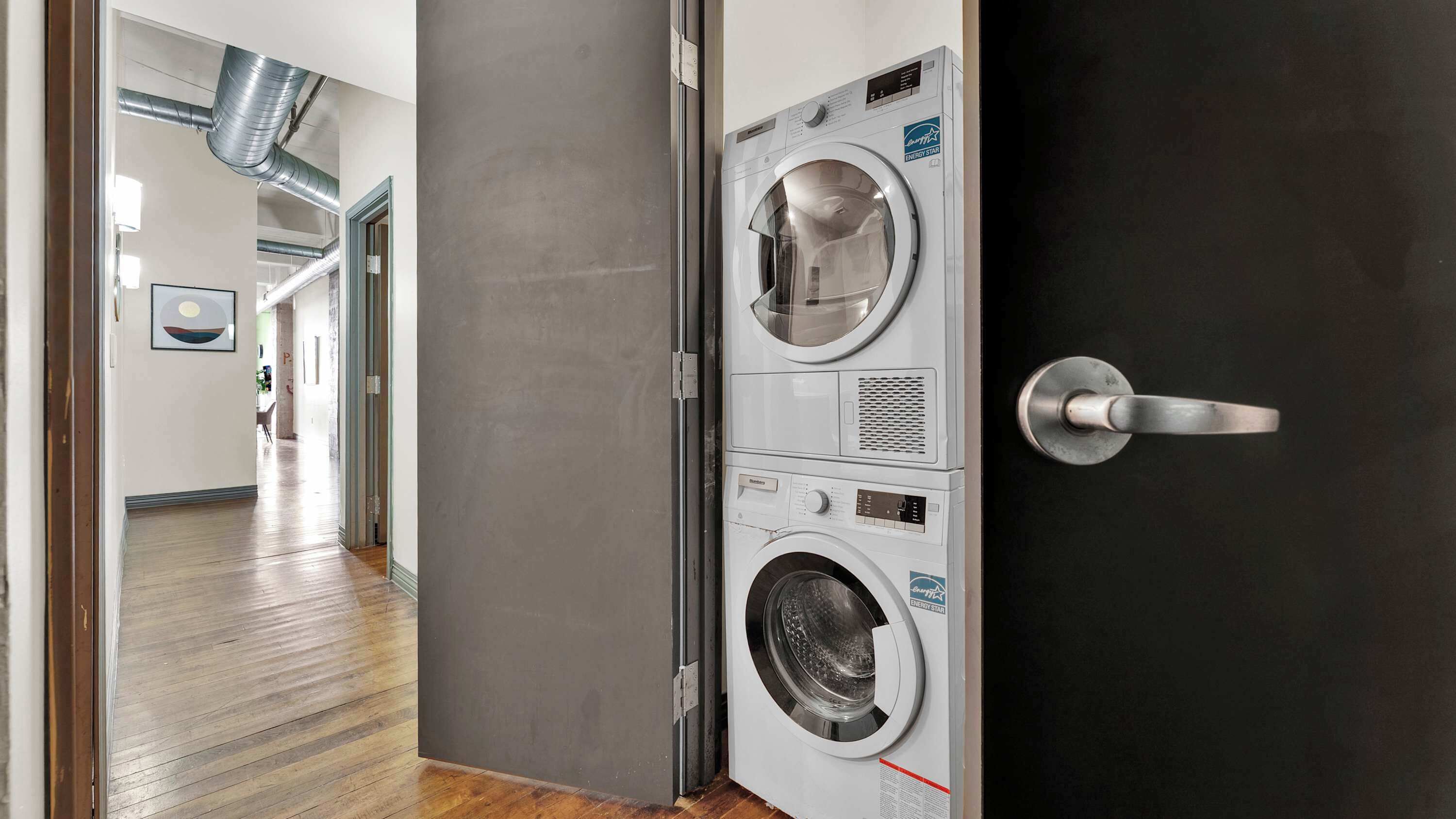 A laundry room with two stacked washing machines and a door to a hallway.