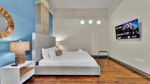 Une chambre d’hôtel moderne avec un grand lit, une table de chevet avec une lampe, un téléviseur fixé au mur et un petit tabouret.