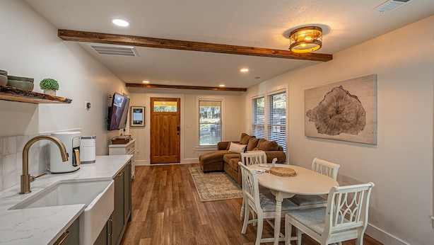 A modern kitchen with a built-in oven, a coffee maker, and a sink. There is a dining area with a white table and chairs.