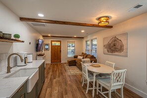 A modern kitchen with a built-in oven, a coffee maker, and a sink. There is a dining area with a white table and chairs.