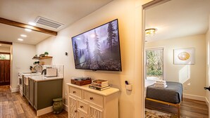 A modern kitchen with wooden flooring, a built-in island, and a flat-screen TV mounted on the wall.