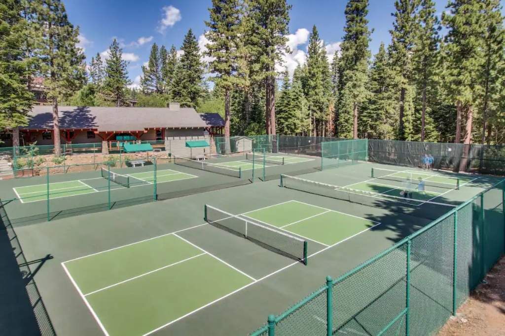 Un complejo de canchas de tenis con varias canchas, rodeado por una cerca verde y árboles altos.