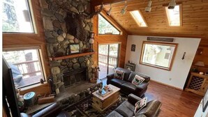 A cozy living room with a stone fireplace, leather sofas, and large windows. - Stunning 3-Bed 2 Bath Cabin with Loft @ Northstar (Truckee)