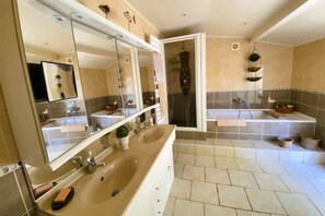 Un baño con un espejo grande, dos lavamanos, una ducha y un mueble de tocador con espacio de almacenamiento.