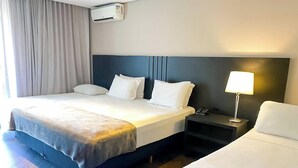 Una habitación de hotel con una cama, mesitas de noche, una lámpara y un equipo de aire acondicionado.