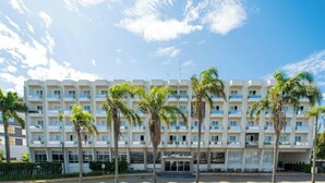 Ein mehrstöckiges Hotel mit einer symmetrischen Fassade, Balkonen und Palmen davor.