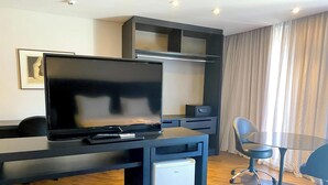 Una habitación de hotel moderna con televisión de pantalla plana, un refrigerador pequeño, una mesa de comedor y una silla.