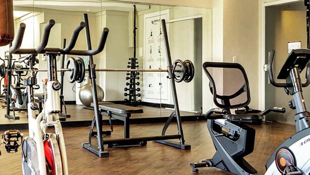 Un gimnasio con equipo de ejercicio, un saco de boxeo y un espejo grande.