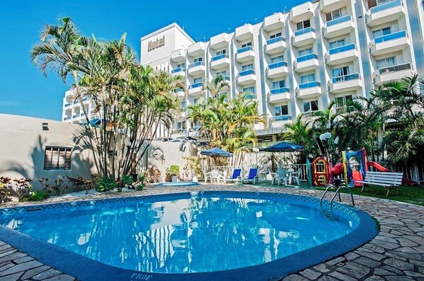 A hotel with a swimming pool, palm trees, and a playground. - Edifício Ponte Hercílio Luz (Florianópolis)