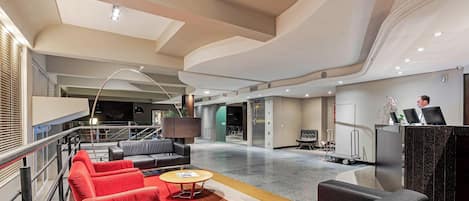 A modern lobby with seating areas, a reception desk, and a staircase.