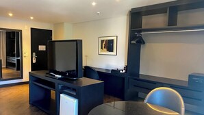 Ein modernes Hotelzimmer mit Fernseher, Schreibtisch, Stuhl und kleinem Kühlschrank.