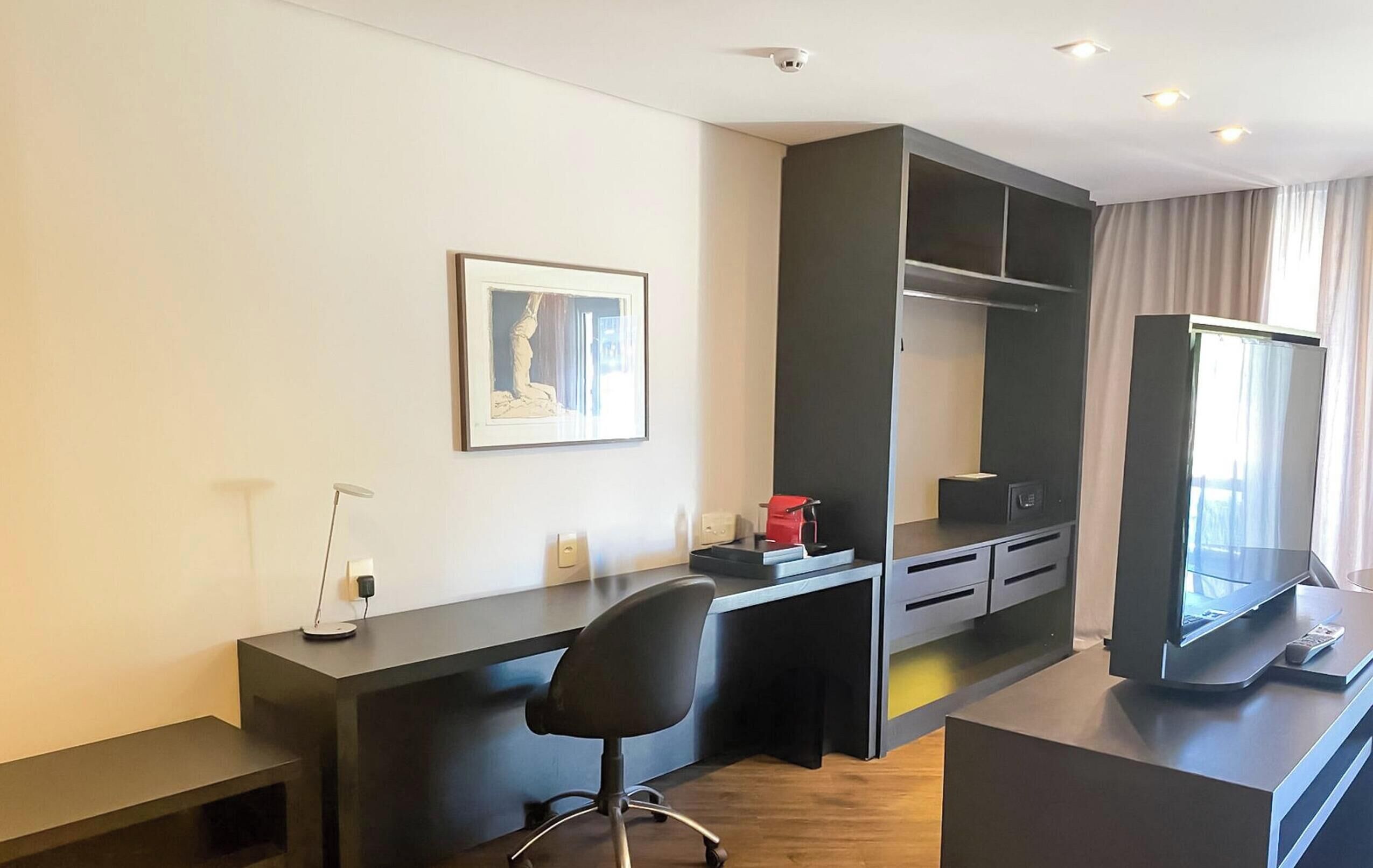 Una habitación moderna con escritorio, silla y un amplio ventanal con cortinas.