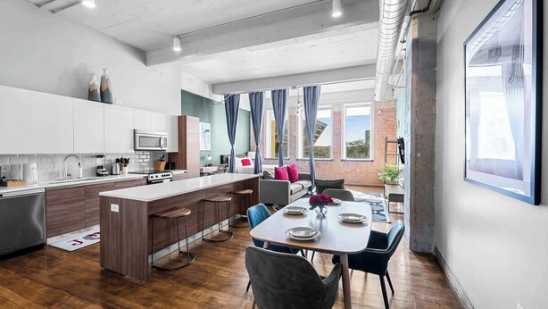 A modern kitchen with white cabinets, a central island, and a dining area with a table and chairs. - Amyfinehouse Loft with Breakfast, Valet, Gym (Dallas)