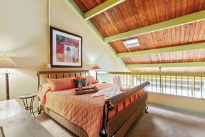 Una camera da letto con soffitto in legno, un letto con testiera in vimini, un quadro appeso alla parete e un balcone con ringhiera.