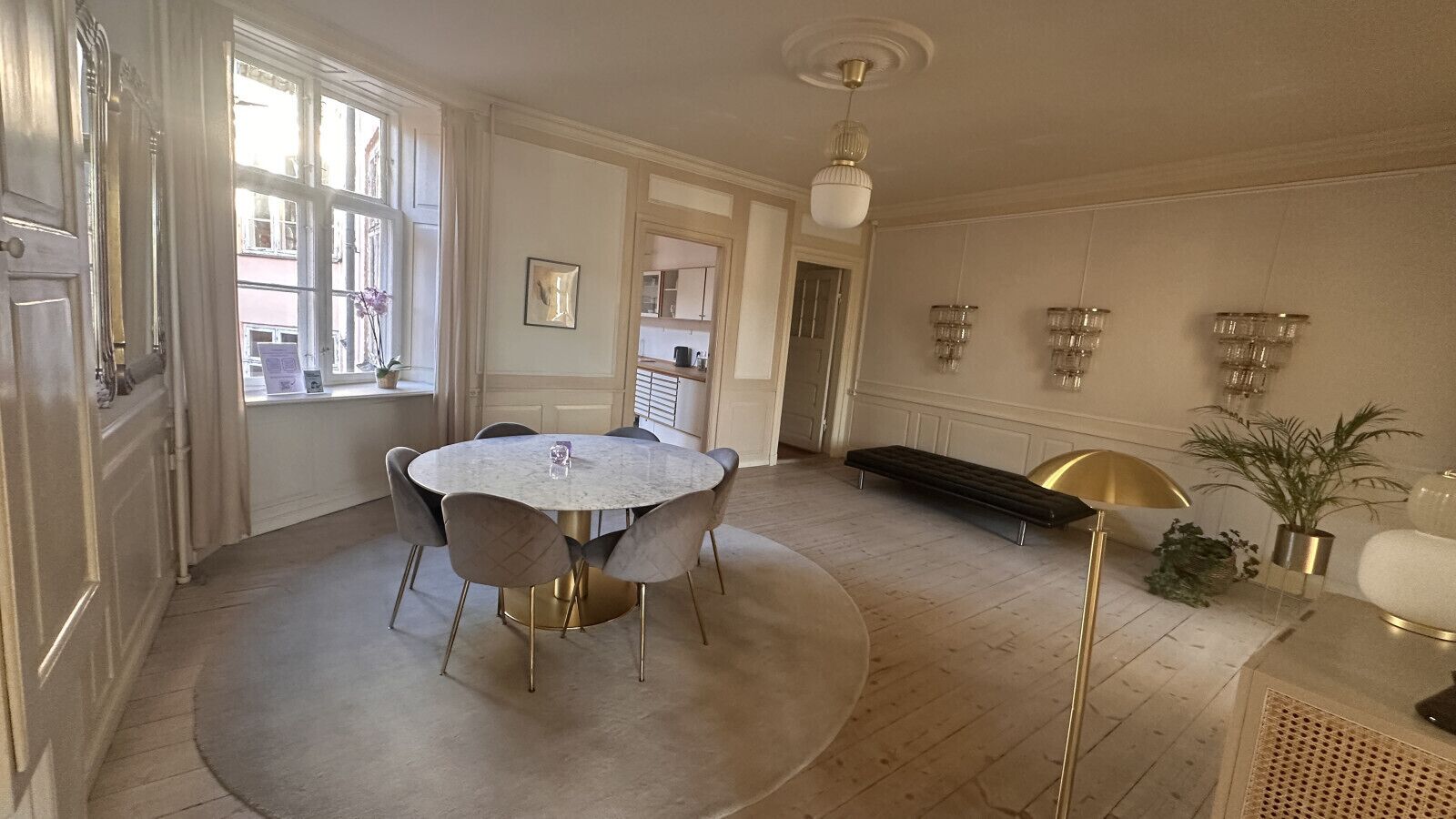 Un espace repas comprenant une table ronde et des chaises, un banc, une plante en pot et un luminaire fixé au mur.