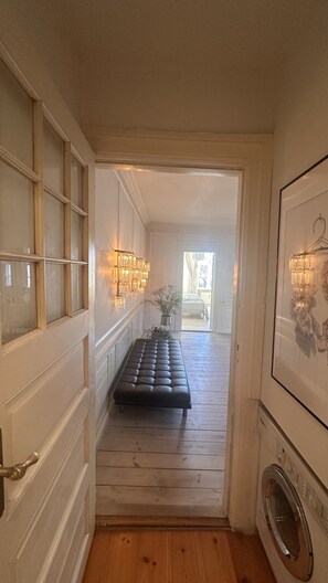 A hallway with a bench, a washing machine, and a chandelier.