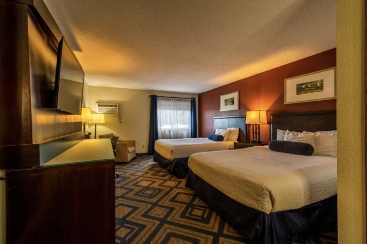 Habitación de hotel con dos camas, un escritorio, un televisor y una ventana con cortinas.