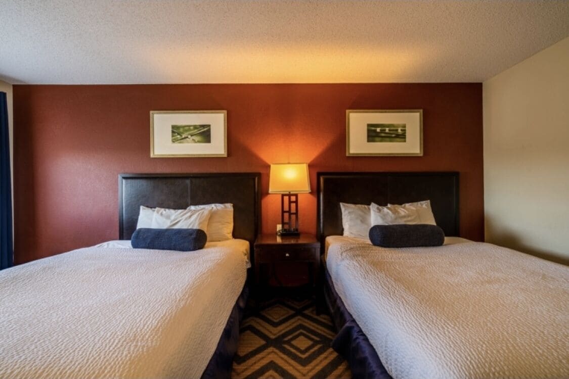 A hotel room with two beds, a nightstand with a lamp, and two framed pictures on the wall.