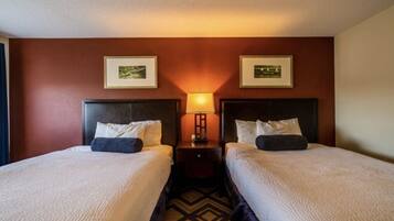 A hotel room with two beds, a nightstand with a lamp, and two framed pictures on the wall.