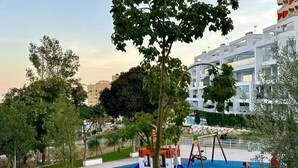 A playground with colorful play equipment, surrounded by trees and a building in the background. - Penthouse with sea view  walking distance to the beach - EL SALTIO (Torremolinos)