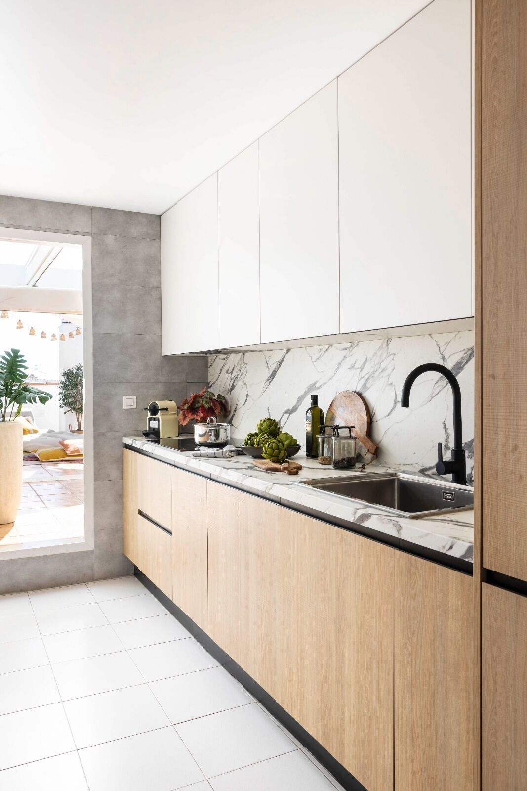 Een moderne keuken met lichte houten kastjes, een marmeren achterwand en een zwarte kraan.