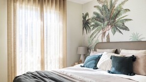 A bedroom with a bed, a nightstand, a lamp, and a wall mural of palm trees. - Penthouse with sea view  walking distance to the beach - EL SALTIO (Torremolinos)