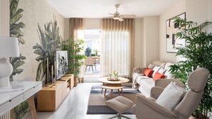 A modern living room with a sofa, armchair, coffee table, and a TV on a wooden cabinet. There are plants, curtains, and a ceiling fan. - Penthouse with sea view  walking distance to the beach - EL SALTIO (Torremolinos)