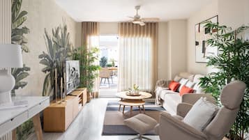 Een moderne woonkamer met een bank, fauteuil, salontafel en een televisie op een houten kast. Er staan planten, hangen gordijnen en er is een plafondventilator.