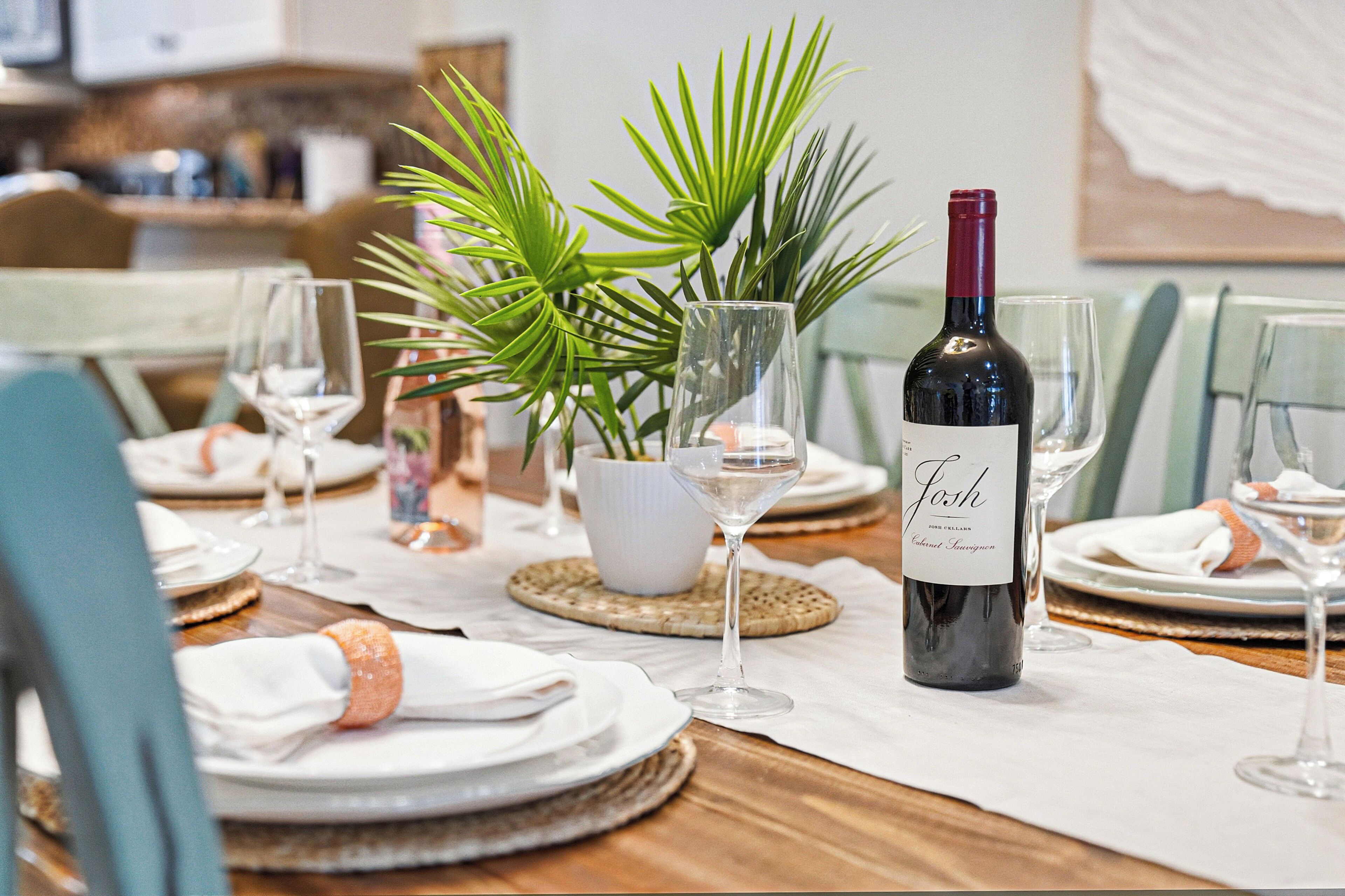 Una mesa lista para comer, con platos, vasos y una botella de vino.
