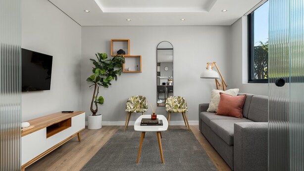 Ein modernes Wohnzimmer mit einem grauen Sofa, einem Couchtisch, einem Fernseher und einem großen Spiegel.