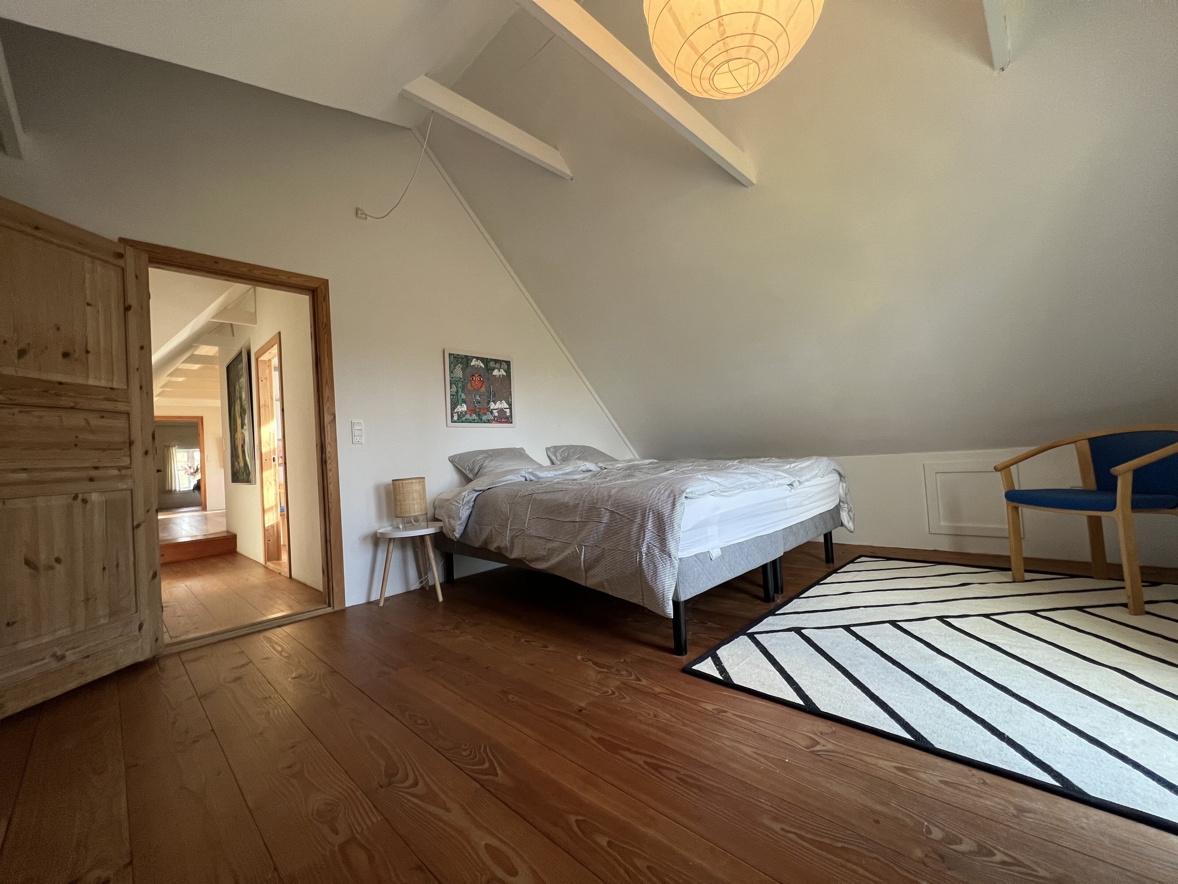 Un dormitorio con cama, una silla, un tapete y un cuadro en la pared.