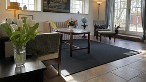 A well-lit living room with a sofa, a coffee table, and a dining table. There are windows with curtains, a globe on the table, and a painting on the wall. - Lake View Apartment (Grindsted)