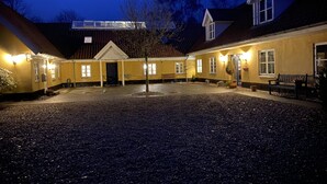 A courtyard with a building featuring a central door, benches, and a tree. - Lake View Apartment (Grindsted)