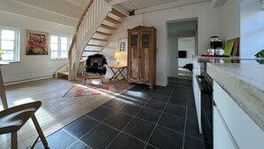 A spacious room with a wooden staircase, a dining area with a table and chairs, and a kitchen area with a coffee maker and a framed picture. - Lake View Apartment (Grindsted)