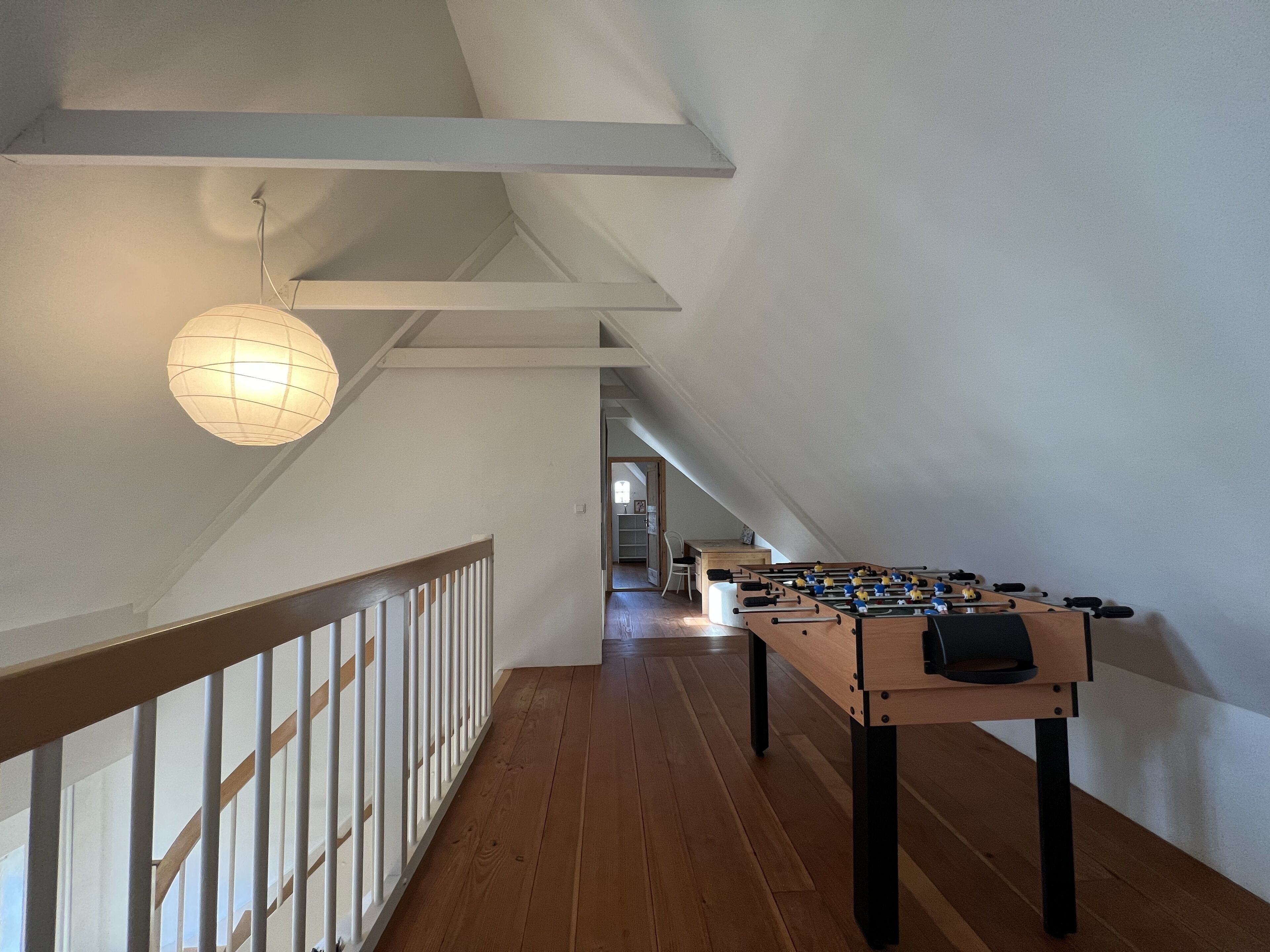 A spacious room with a wooden floor, a foosball table, and a hanging light fixture.
