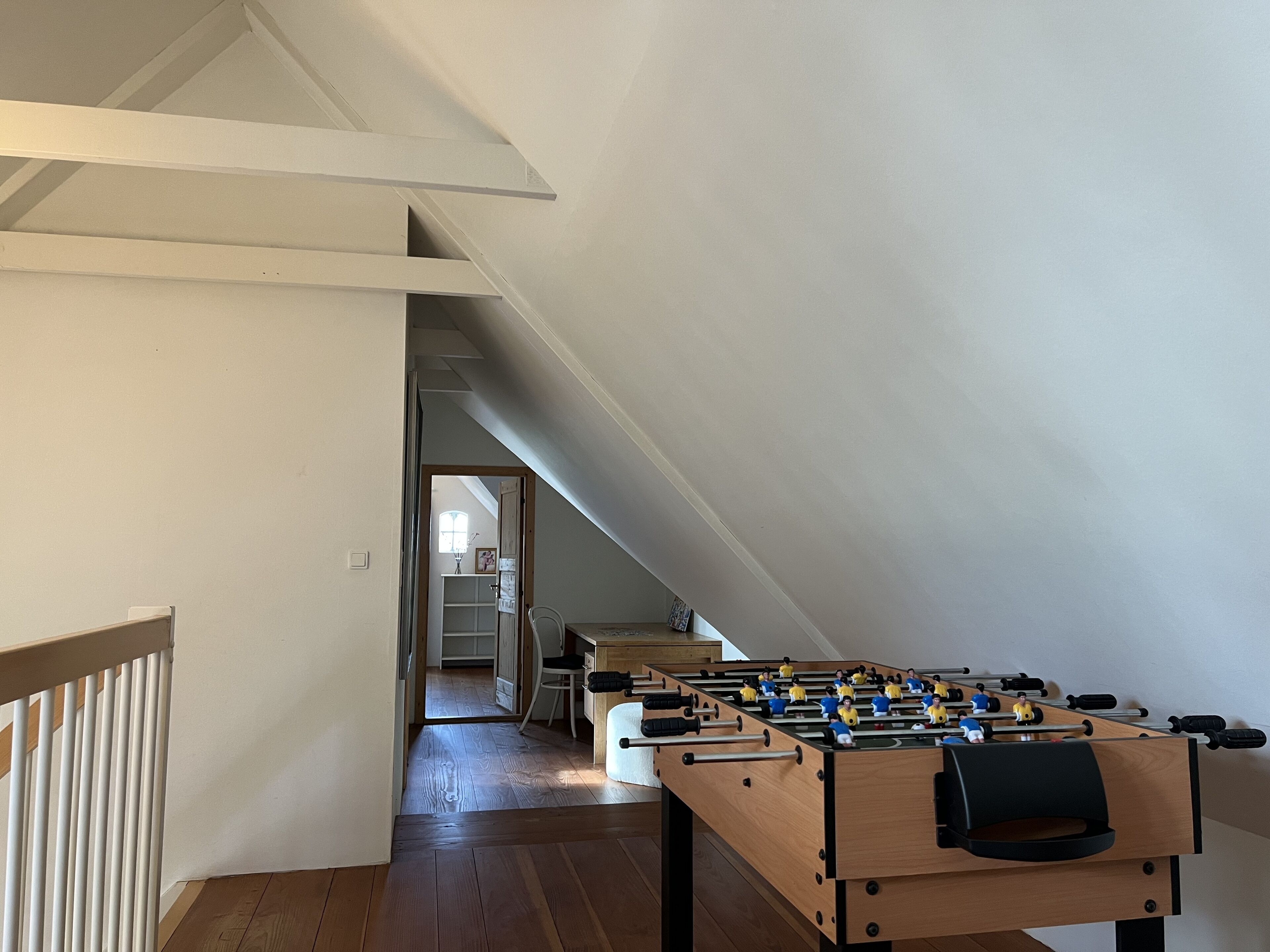 A room with a foosball table, wooden flooring, and a sloped ceiling.