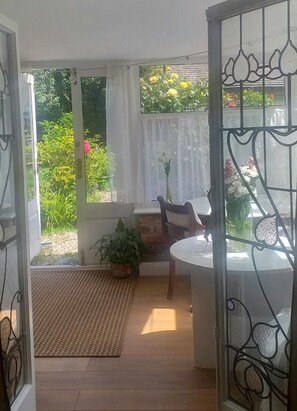 A sunlit room with a view of greenery outside, a small table with a chair, and a potted plant.