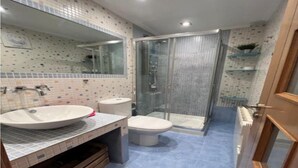 Ein Badezimmer mit großem Waschbecken, Toilette und einer Duschkabine aus Glas.