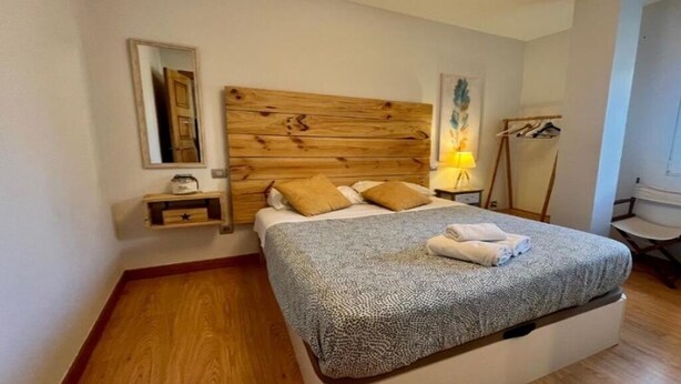 Ein Schlafzimmer mit hölzernem Kopfteil, einem Bett mit gemustertem Überwurf, einem Nachttisch mit Lampe und einem Kleiderständer.