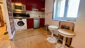 Eine kompakte Küche mit Waschmaschine, Geschirrspüler und einer kleinen Essecke mit Hocker.