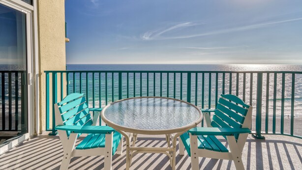 Ein Balkon mit Glastisch und zwei Stühlen mit Blick auf einen Strand.