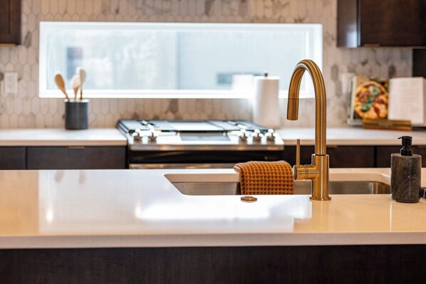 A modern kitchen with a stainless steel sink, a gold faucet, and a marble countertop.