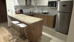 A modern kitchen with a central island, bar stools, stainless steel appliances, and white cabinetry. - Aparts4Days Miraflores Down Town 1 or 3 Bedroom Apartment (Lima)